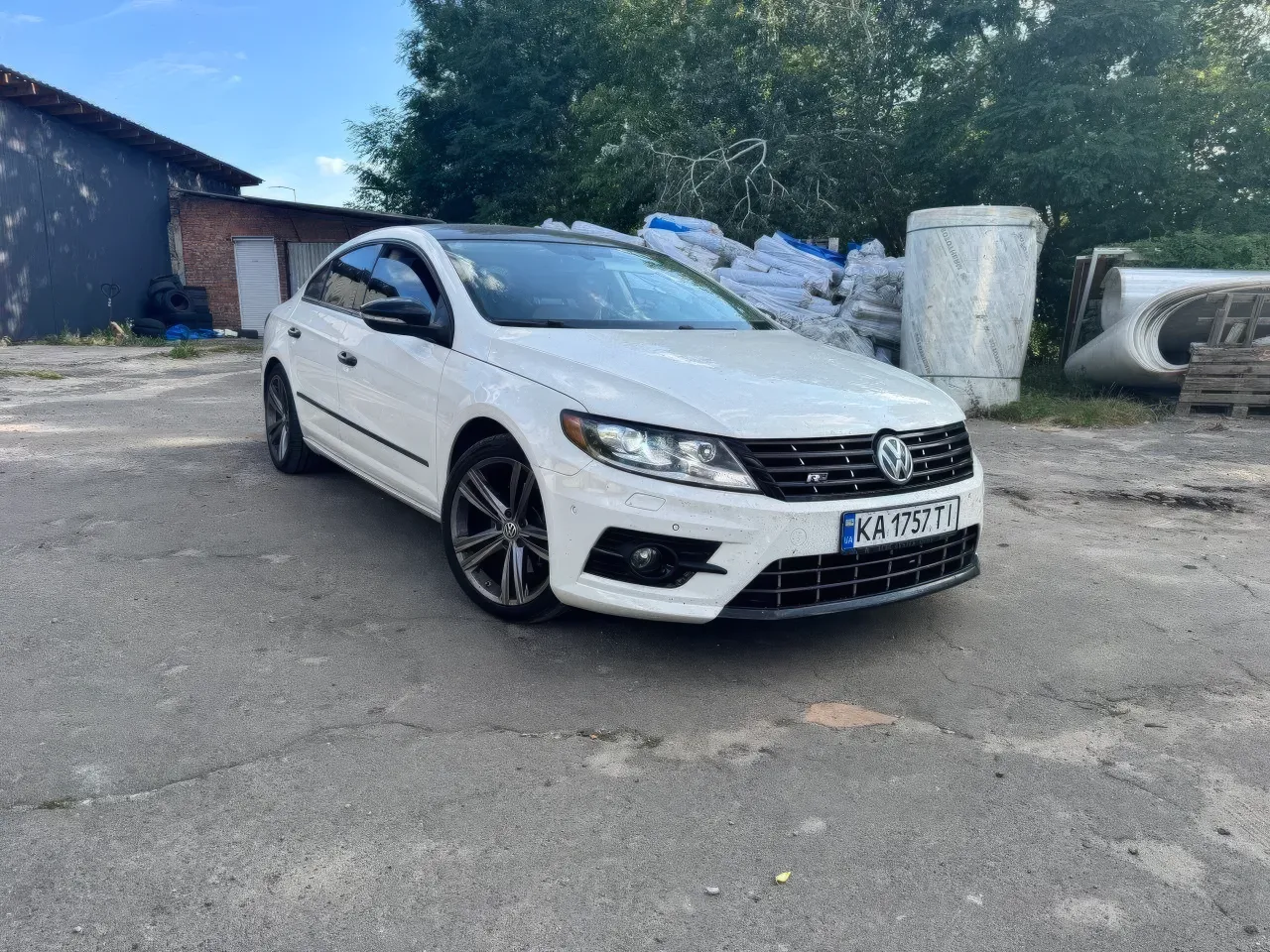 На відкритому майданчику сфотографовано чистий білий Volkswagen Passat CC у спортивному виконанні R-Line. Людей у кадрі немає. Яскраве денне світло добре підкре